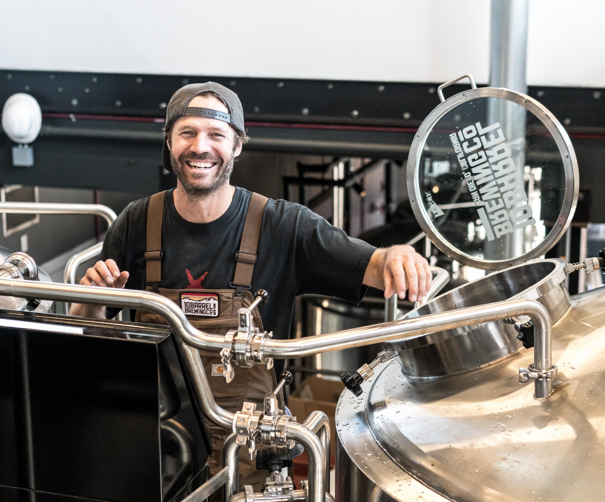 Brewer standing by equipment in a brewery, smiling
